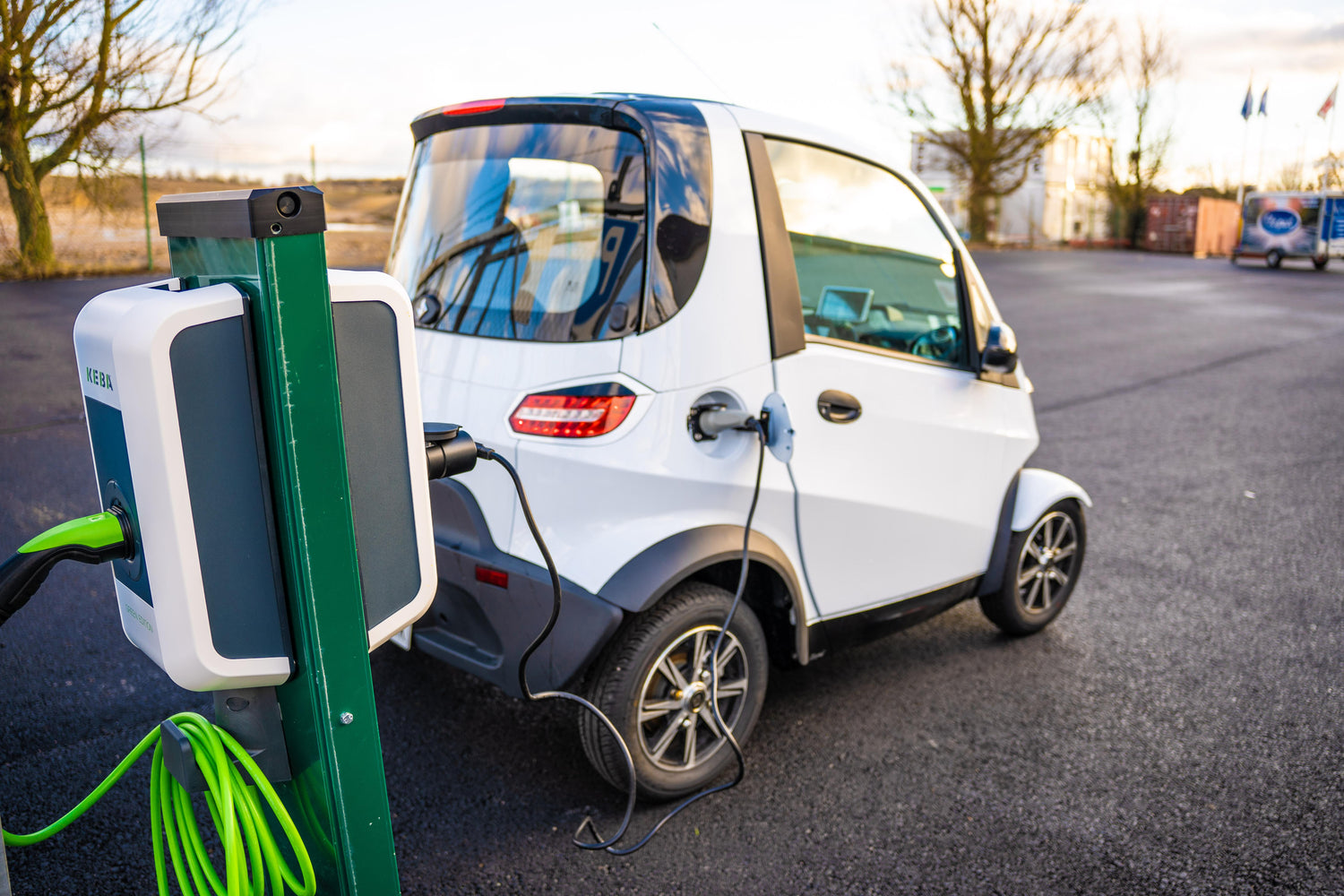 Vit elmopedbil som laddas i laddstolpe med adapter